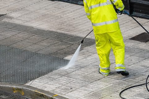 Worker cleaning the sidewalk with pressurized water. Maintenance or cleaning concept