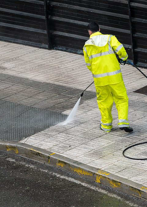 Worker cleaning the sidewalk with pressurized water. Maintenance or cleaning concept